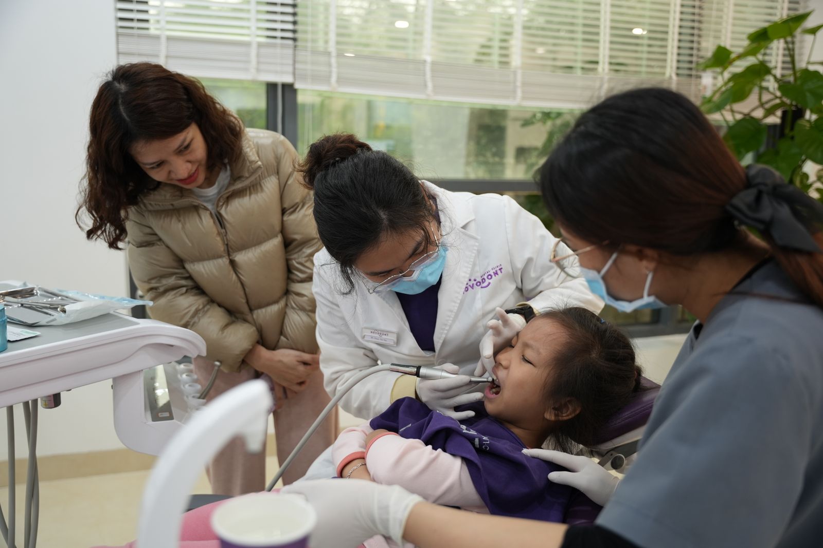Dentist examining a young girl's teeth while her parent watches